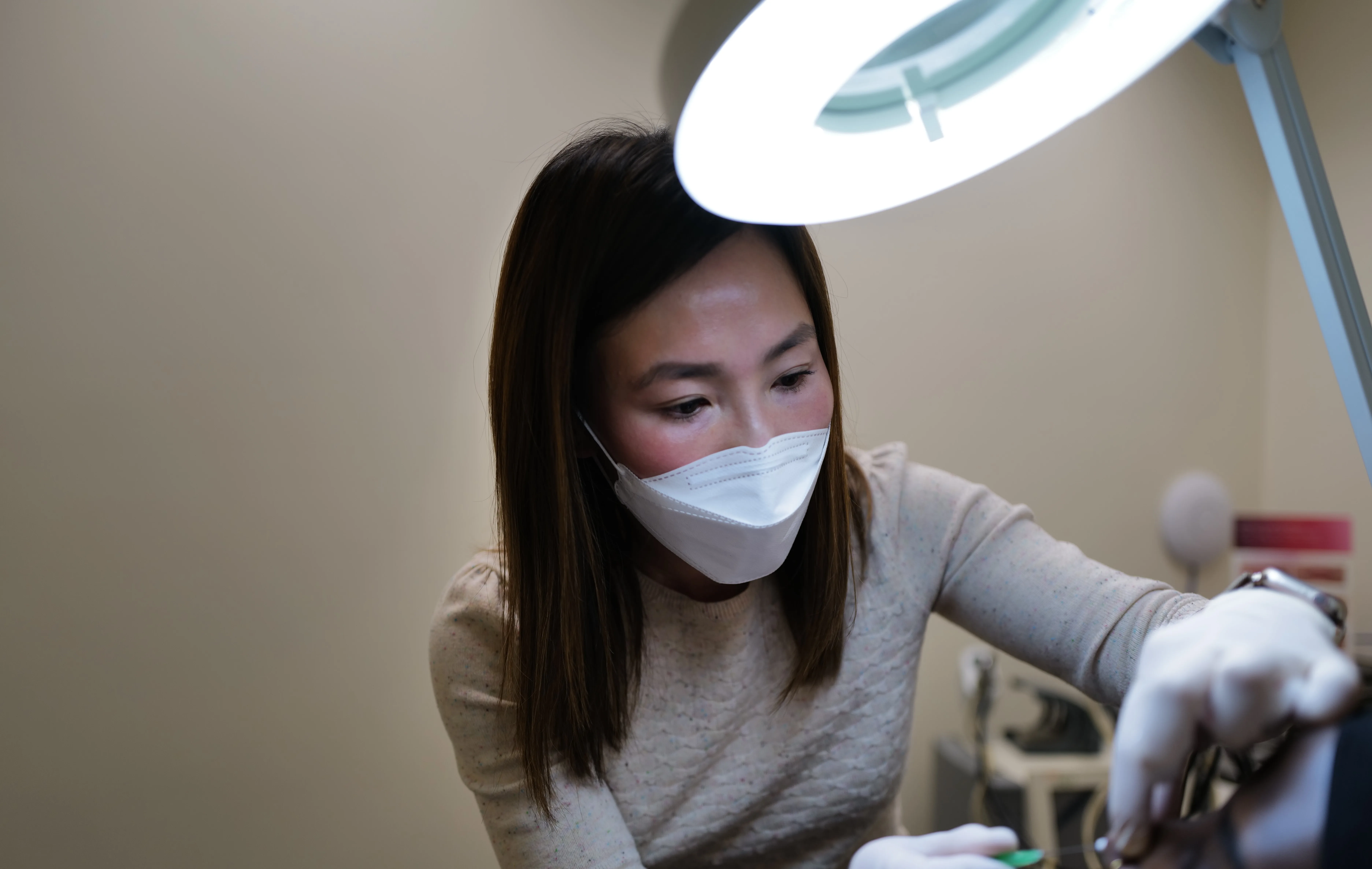 Masked clinician working under a magnifying lamp at HEMAC